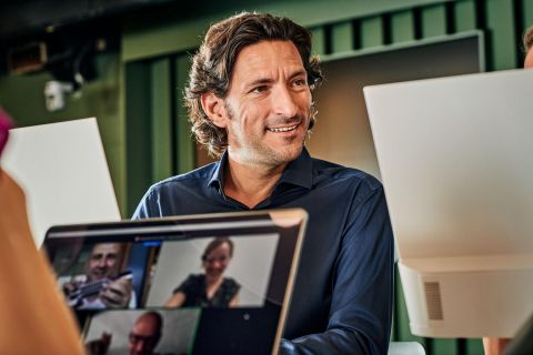 Mann in Videokonferenz; im Vordergrund eine laufende Konferenz